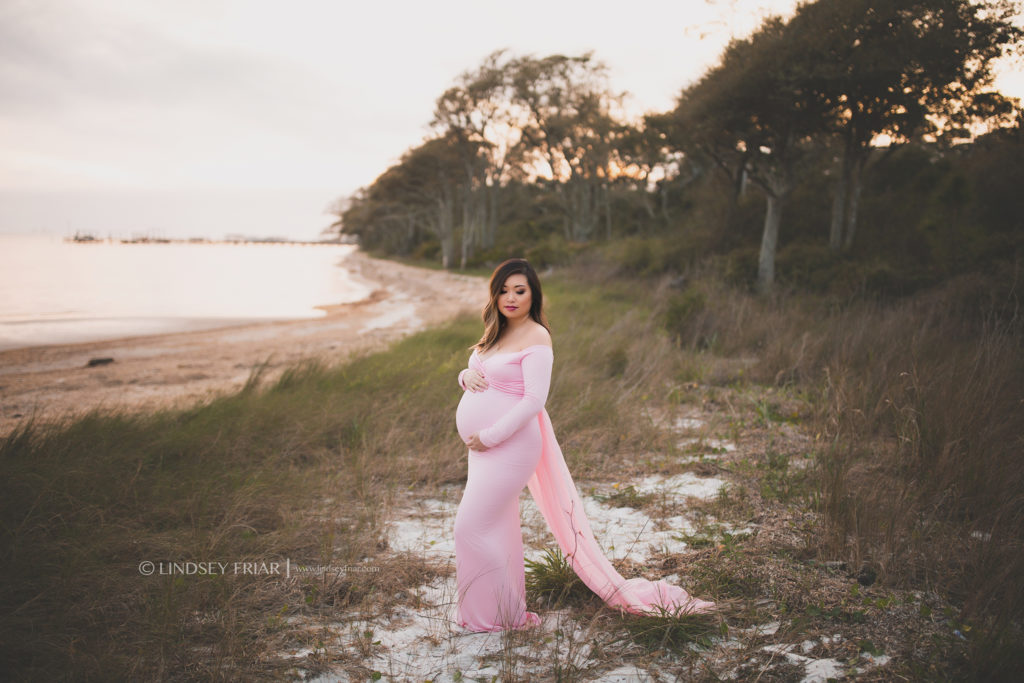 mama to be wearing a long flowy dress on a grassy shore