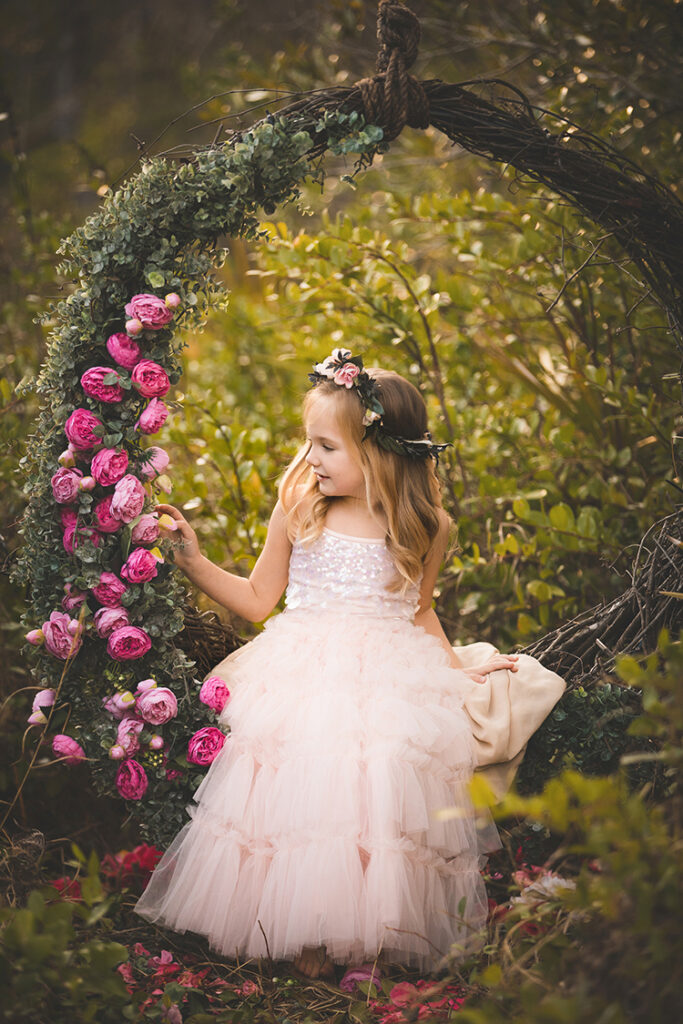 little girl in a pink sequined gown looking at the flowers on her swing