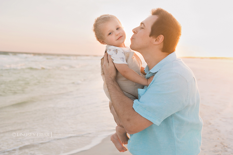 dad trying to kiss his little boy who is pulling away from him