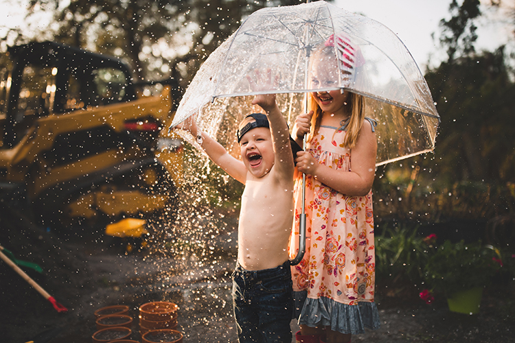 boy and girl standing under a clear umbrella getting sprayed by water